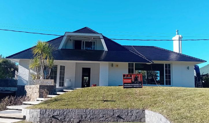 Casa con techo oscuro recién limpio y cartel de J.M en el jardín